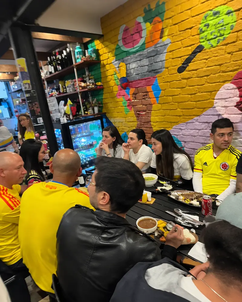 A full dining room at Tentaciones during an event, many people in yellow Colombia shirts under a painted mural
