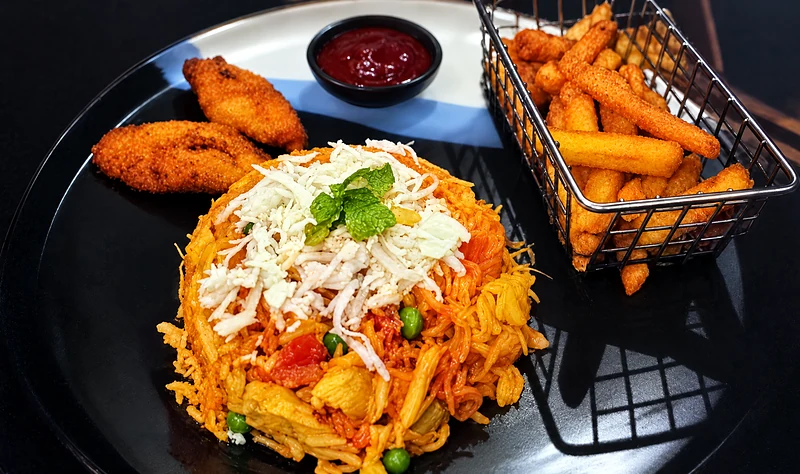 Arroz con pollo with shredded cheese on top, fried plantain and a basket of chips