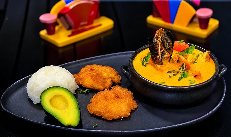 Cazuela in a clay pot with rice, avocado and crisp patacones