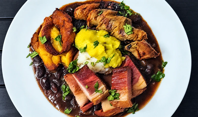 Cazuela de frijol: bean stew with chicharron, chorizo, ripe plantain and avocado in a white bowl