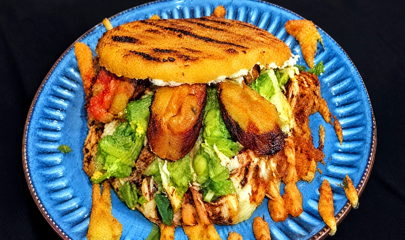 Chori Arepa on a blue plate with chorizo, pulled pork, guacamole and cheese