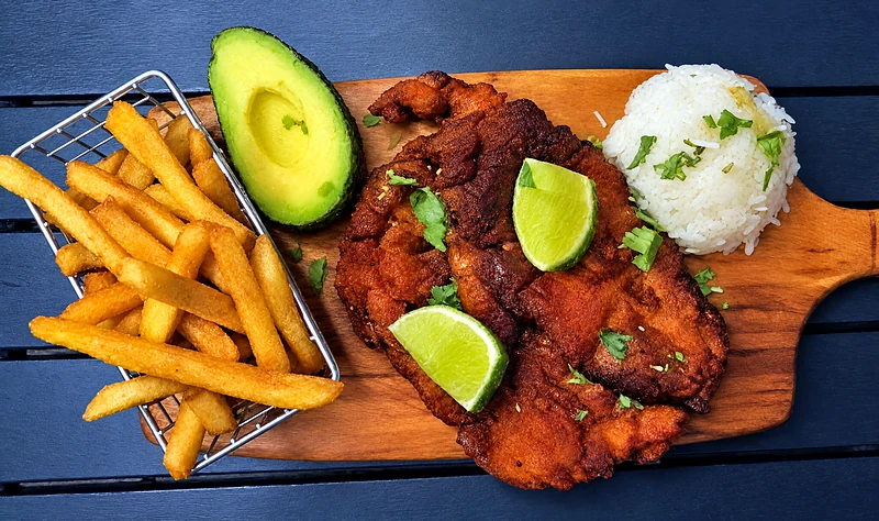 Chuleta valluna: crumbed pork schnitzel on a board with chips, rice, avocado and lime
