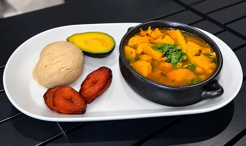Mondongo stew in a black clay pot with rice, avocado and fried plantain