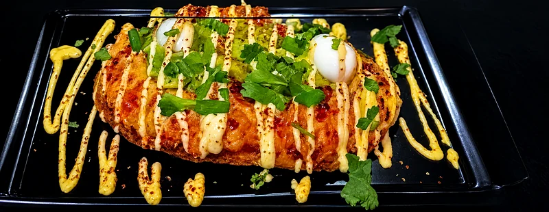 Patacon pisado on a black tray, topped with meat, cheese, quail eggs, coriander and salsa