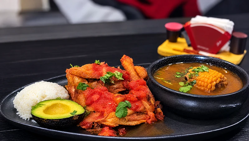 Sancocho de gallina: a bowl of broth with corn next to hen, rice and avocado